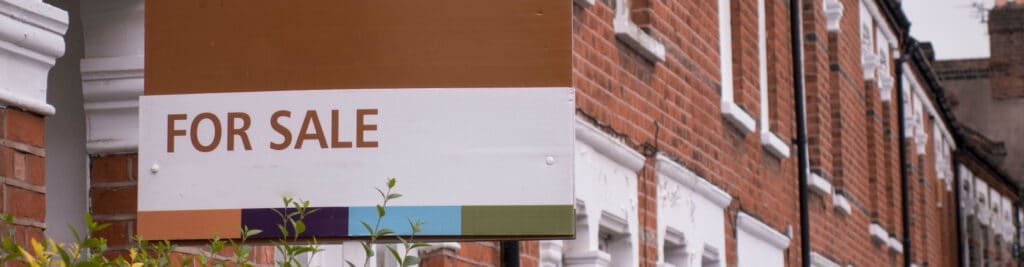 A “for sale” sign outside a row of red brick terraces